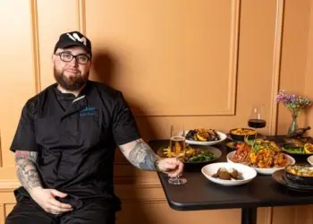 Chef Matt Price of Fraiche DC poses with a spread of dishes on a table at his restaurant