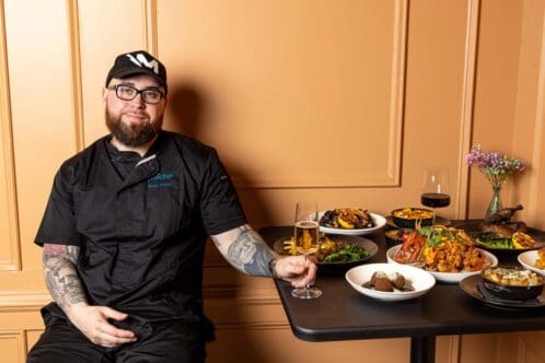 Chef Matt Price of Fraiche DC poses with a spread of dishes on a table at his restaurant