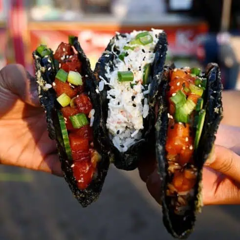 Two hands holding three sushi tacos from Taco Nori at the Richmond Night Market in British Columbia.
