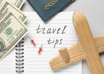 Notebook with text TRAVEL TIPS, wooden airplane and money on light background, closeup. Itinerary concept