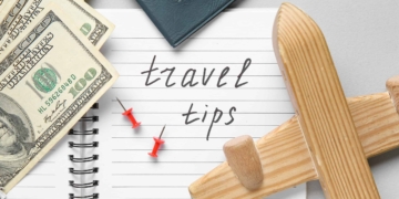 Notebook with text TRAVEL TIPS, wooden airplane and money on light background, closeup. Itinerary concept