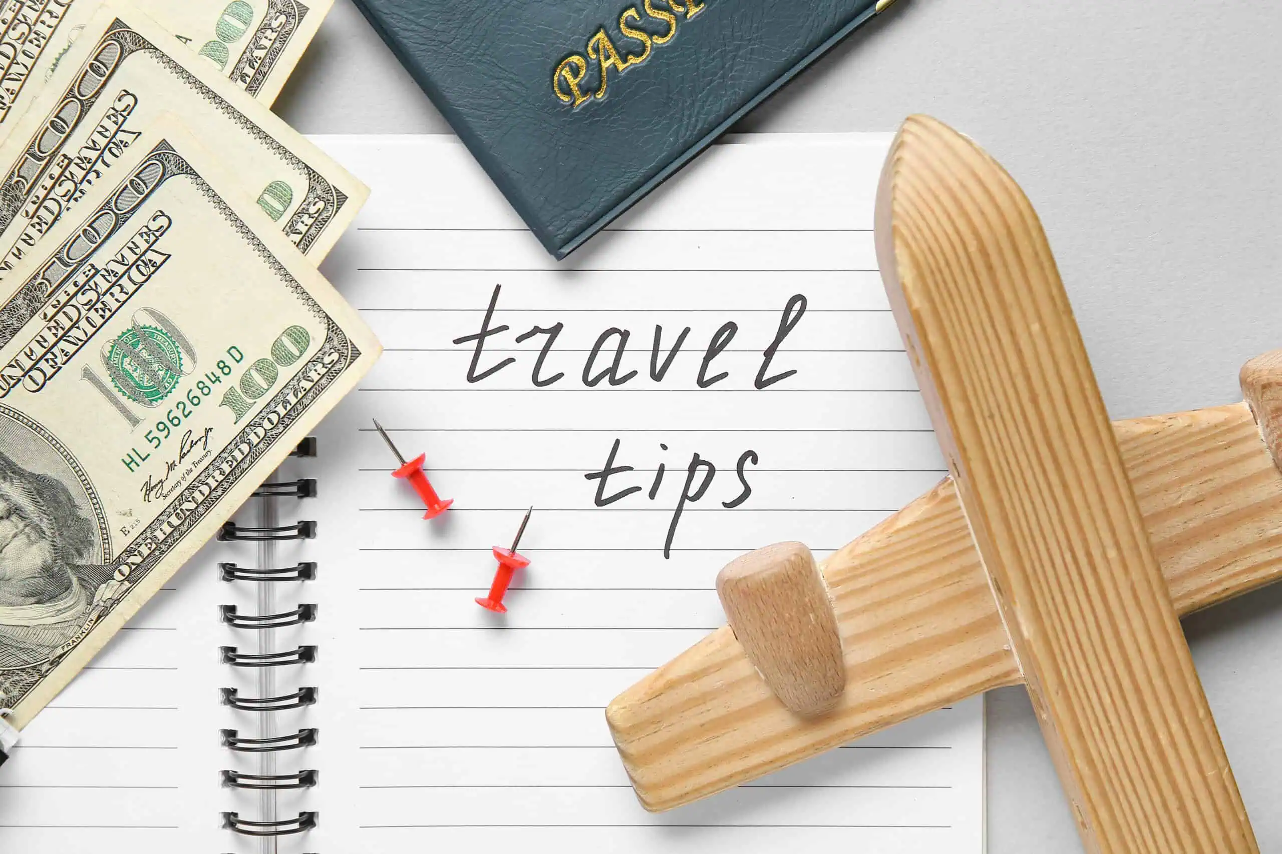 Notebook with text TRAVEL TIPS, wooden airplane and money on light background, closeup. Itinerary concept